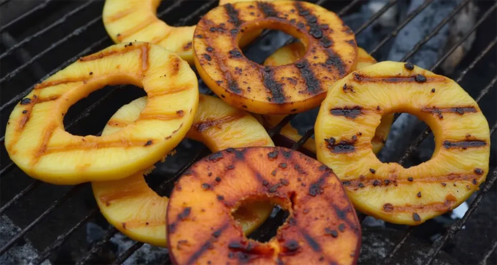 Grilled pineapple and peaches on a campfire grill.