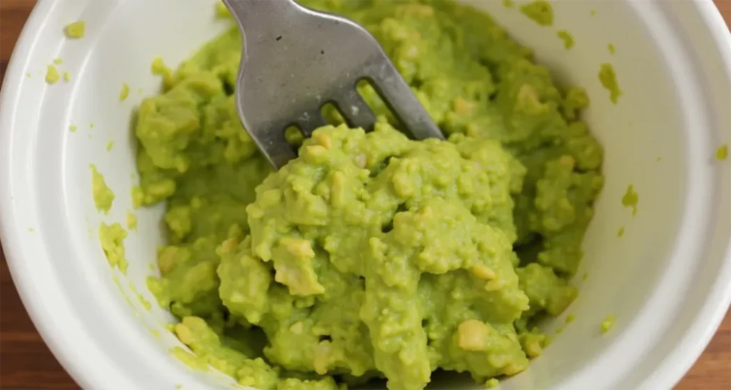 Mashing avocado in a bowl with a fork to create a creamy base.