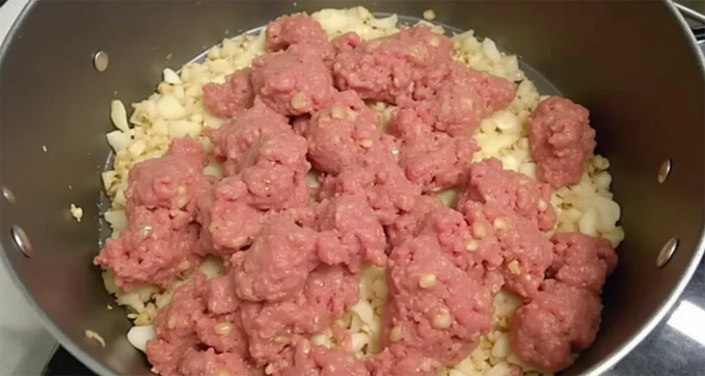 Ground meat browning in a pot with onions and garlic over medium heat.