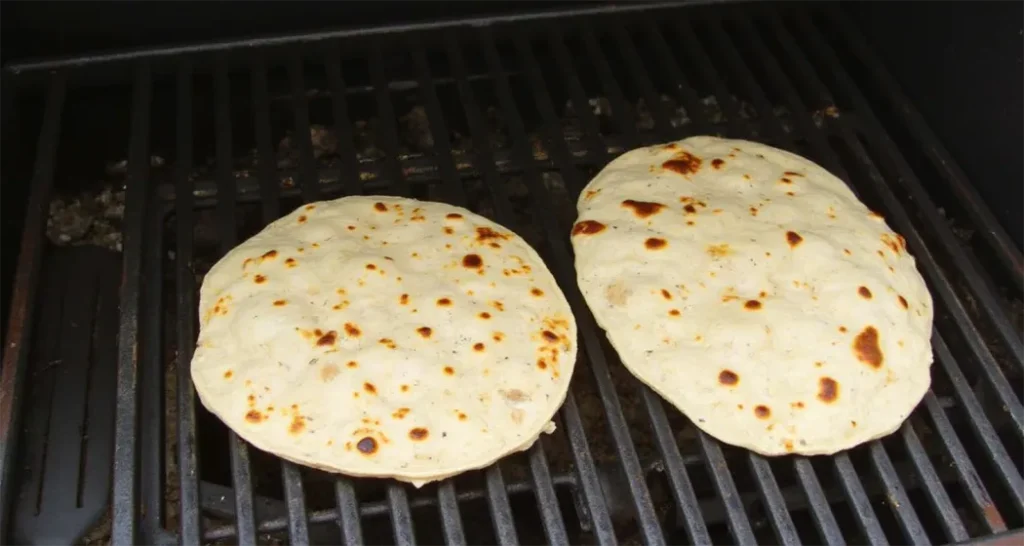 Tortillas warming directly on a campfire grill.